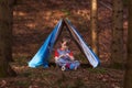 Boy sitting under a play tent in the woods playing alone in solitude enjoying creating a bow play pretending.