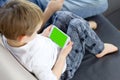 Boy sitting and using mobile smart phone with green screen at home. Close up of thumb scrolling up through touch screen display