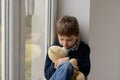 Boy sitting on the windowsill and hugs his favourite teddy bear Royalty Free Stock Photo