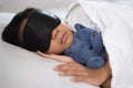 Boy sleeping on bed with teddy bear white pillow and sheets wearing sleep mask Royalty Free Stock Photo