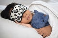 Boy sleeping on bed with teddy bear white pillow and sheets wearing sleep mask Royalty Free Stock Photo