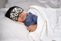 Boy sleeping on bed with teddy bear white pillow and sheets wearing sleep mask Royalty Free Stock Photo