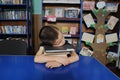 Boy sleeping in library exausted, putting head on pile of book Royalty Free Stock Photo