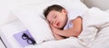 The boy is sleeping in a white bed, next to the pillow is a book with glasses Royalty Free Stock Photo