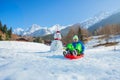 Boy slide downhill alpine slope on sledge passing by snowman
