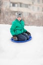 Boy slides down the hill on snow saucer against the background of multi-house. Seasonal concept. Winter day