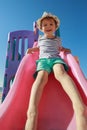 Boy sliding down playground pink slide, in a blue sky background Royalty Free Stock Photo