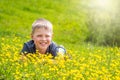 A boy with a smile is resting on a green lawn with yellow wildflowers in the sun and looking up Royalty Free Stock Photo