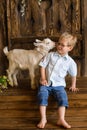 Boy smiles on wooden steps of the porch next to newborn goaling and hugs him