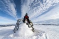 Boy in snowmobile driver clothes sits on the big stone point marking Swedish Norwegian state border in Lappland.