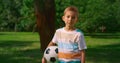 Boy with soccer ball posing camera on nature. Serious little athlete closeup.