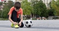 Boy soccer player tying shoelaces and soccer ball near him in town square Sports games and leisure outside concept Royalty Free Stock Photo