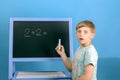 The boy solves the math equation 2 + 2 written on the blackboard. The child does not know the answer to simple examples Royalty Free Stock Photo