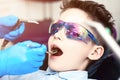 A boy in special glasses in the dentist`s chair. the doctor in sterile gloves shows him his smile in the mirror