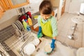 Boy sponging bowls under running water in the sink