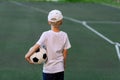 A boy in sports clothes sitting on a green lawn on a football field with a soccer ball back, back view, sports section, training