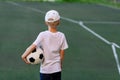 A boy in sports clothes sitting on a green lawn on a football field with a soccer ball back, back view, sports section, training