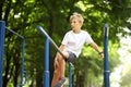 A boy on a sports ground in a park climbed onto a sports equipment and looks while sitting on it