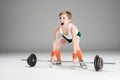 Boy in sportswear training with barbell on grey