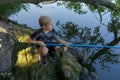 A boy squats on rocks and catches fish. Sport fishing on the river in summer Royalty Free Stock Photo