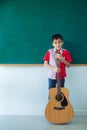 Boy stading with guitar in front of blackboard Royalty Free Stock Photo