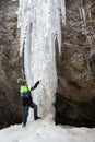 Boy stand at the bottom of frozen waterfall and touch white icicles.