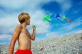 Boy stand holding many kites over sky at pebble beach Royalty Free Stock Photo