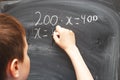Boy standing back in front of school blackboard and writing. Schoolboy solves math example at the chalkkboard