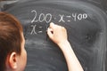 Boy standing back in front of school blackboard and writing. Schoolboy solves math example at the chalkkboard Royalty Free Stock Photo