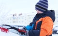 The boy standing near the car and holding a brush. The child cleans the car from snow.