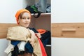 Boy standing near messy clothes on shelf. Messy home kid`s room. Boy thinking what to do with messy