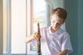 The boy is standing by the window with a black clarinet. Musicology, music education and education. Royalty Free Stock Photo