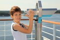 Boy stands on board of ship near binoculars