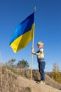 boy stands on a hill against a blue sky with a large waving blue-yellow Ukrainian flag Royalty Free Stock Photo