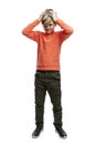 The boy stands and holds his head with his hands. A 9 year old boy in an orange sweater and green trousers. Full height.