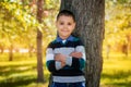 A boy stands leaning against a tree in a park Royalty Free Stock Photo