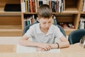 A boy stands in the library and reads a book while standing. Preparing for homework. The boy loves to read. Free space at the Royalty Free Stock Photo