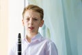 The boy stands near the window and holds a black clarinet in his hands, looks into the camera. Musicology, music education and edu Royalty Free Stock Photo