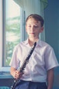 The boy stands near the window and holds a black clarinet in his hands, looks into the camera. Musicology, music education and edu Royalty Free Stock Photo