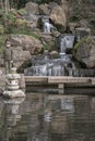 A boy stands on a stone bridge in front of waterfall and rocky cliffs in Kyoto garden Royalty Free Stock Photo