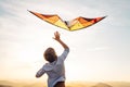 Boy start to fly bright orange kite in the sky