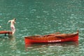 A Boy Steps Off the Red Dock into a Green Sea, Red Row Boat Drifts Nearby Royalty Free Stock Photo