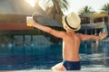 A boy in a straw hat with a cocktail in hand sitting on the pool