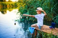 Boy in straw hat with a fishing rod catches fish on riverbank at golden hour of sunset, river Royalty Free Stock Photo