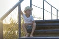 Boy in a straw hat sitting on wooden stairs outdoors at sunset. Holiday Royalty Free Stock Photo