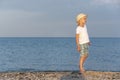 Boy in straw hat walks along the seashore in rays of sunset. Carelessness