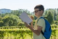 Boy on the street reading a book and eating an apple.