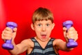 A boy in a striped t-shirt goes in for sports with purple dumbbells on a red background