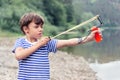 Boy in a striped t-shirt shoots a slingshot, side view
