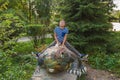 Boy in a striped t-shirt sits on a dinosaur statue in the park at the playground
